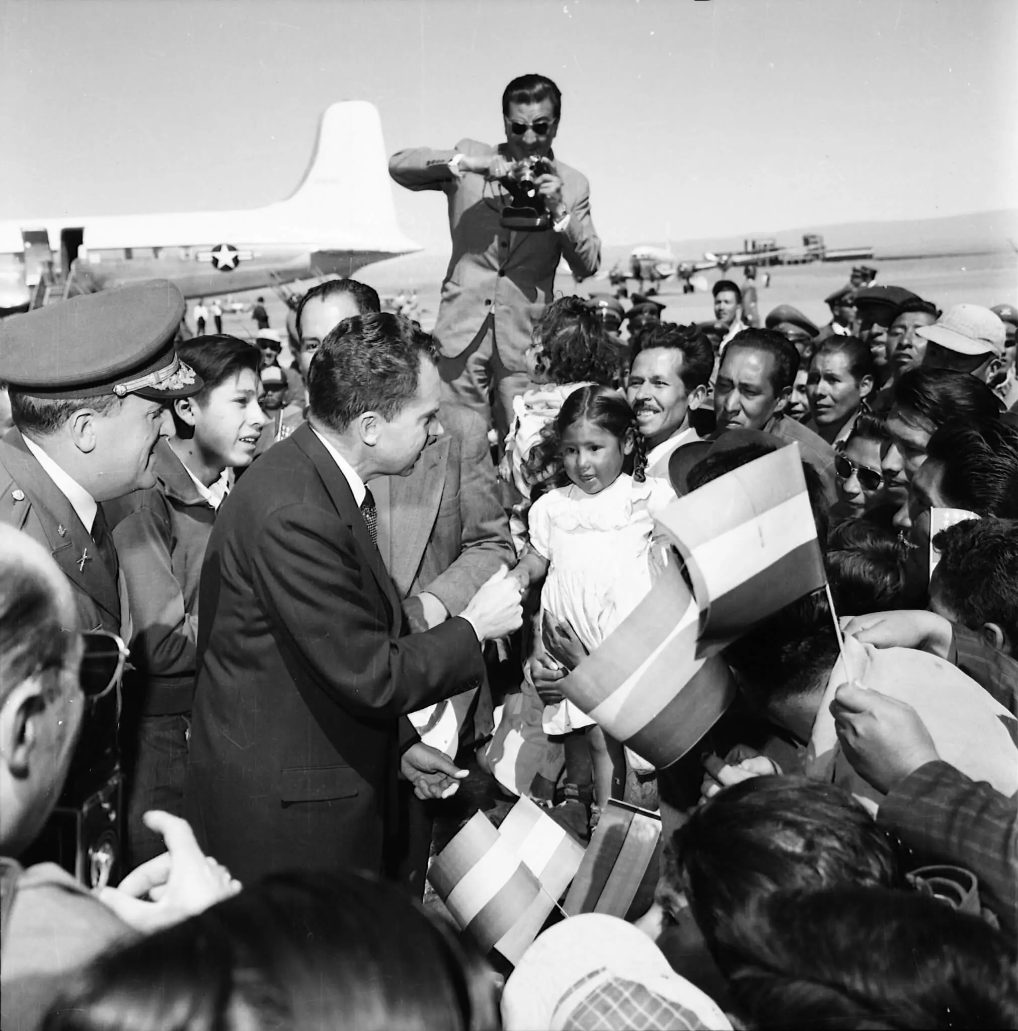In seiner Funktion als US-Außenminister absolviert Richard Nixon im Mai 1958 einen Staatsbesuch in Bolivien. Noch am Rollfeld wird er von Journalisten und einer begeisterten Menge begrüßt. Im Hintergrund ist der Flieger von Nixon zu sehen.