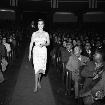 Vera Miles und John Wayne sind anläßlich einer Filmpremiere in La Paz anwesend. Hier schreitet Vera Miles zum Podium eines Kinos, wo sie auch eine Rede halten wird. Wahrscheinlich wurde der Western „The Searchers“ gezeigt, in dem Vera Miles und John Wayne im Jahr 1956 die Hauptrollen gespielt haben.